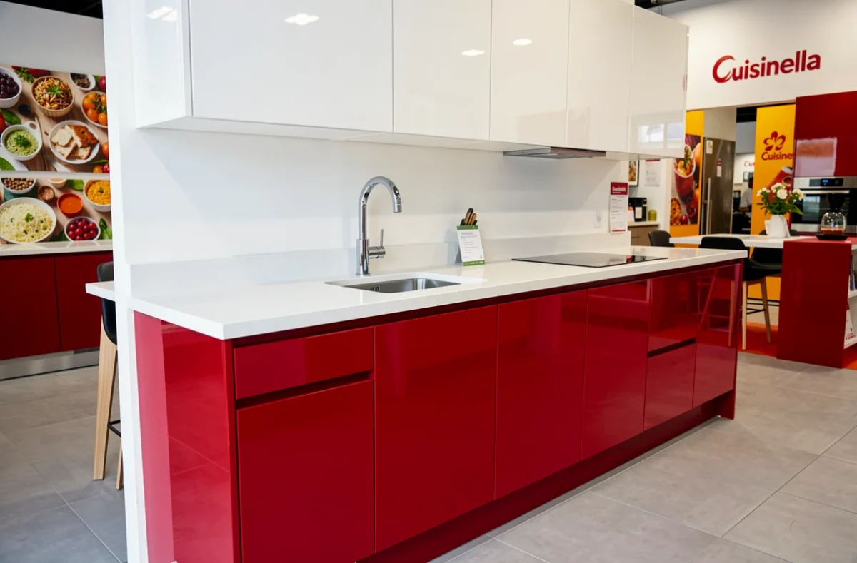 Cuisine Cuisinella bicolore avec bas rouge brillant et hauts blancs, plan en quartz poli dans un showroom moderne